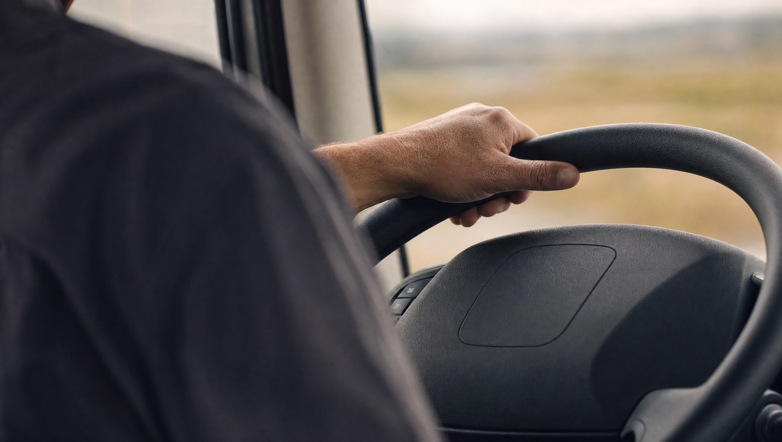 Detalhe da mão de um motorista segurando o volante de um caminhão, sob luz natural